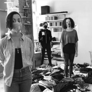 5 members of the Third Root team pose facing the camera in the community room, socially distanced and wearing masks, with donated items strewn about the floor. The photo is black and white.